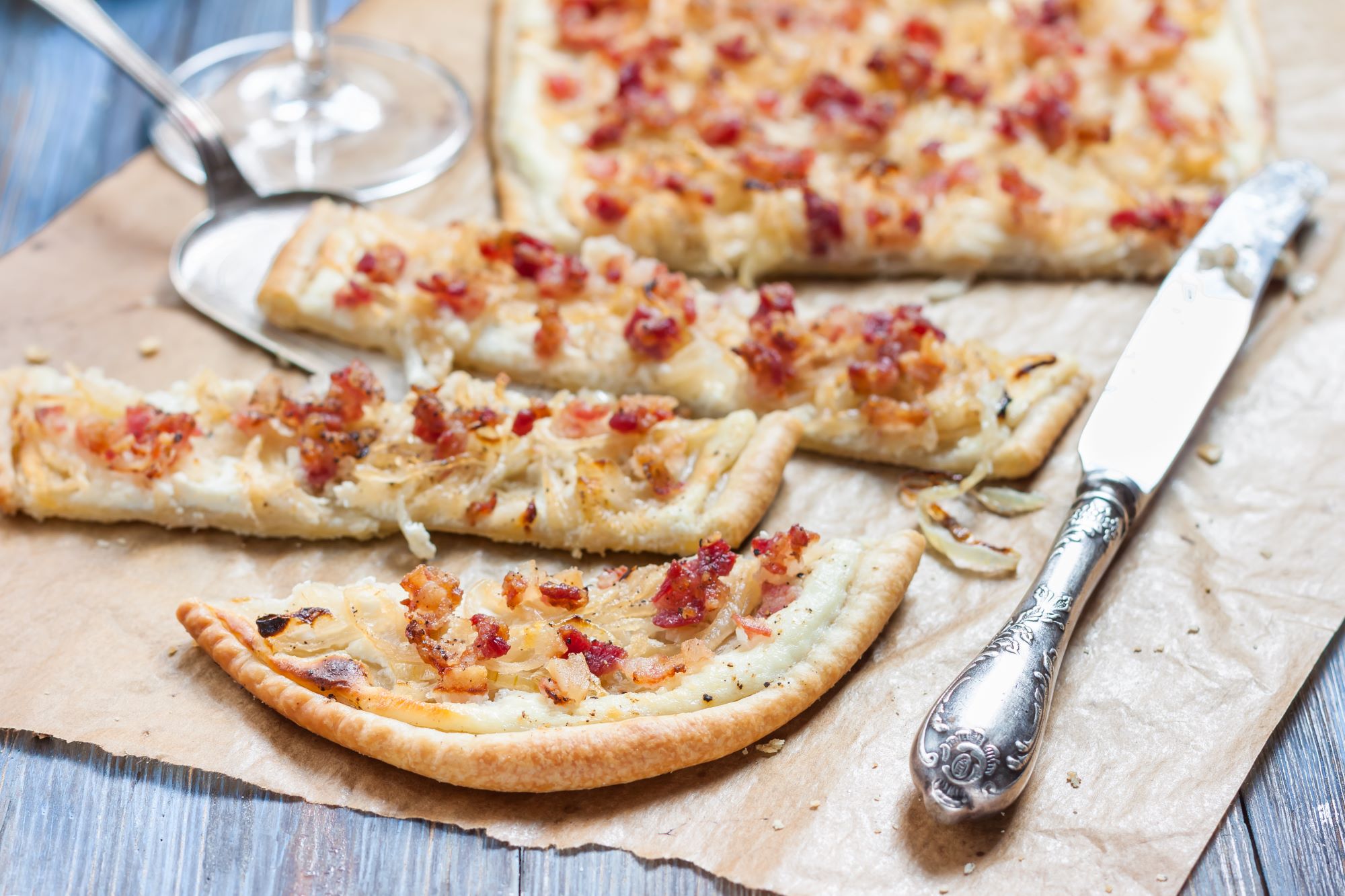 Postrežena in narezana značilna alzaška jed Flammekueche - tanko testo, obloženo s kislo smetano, sirom, čebulo in slanino.