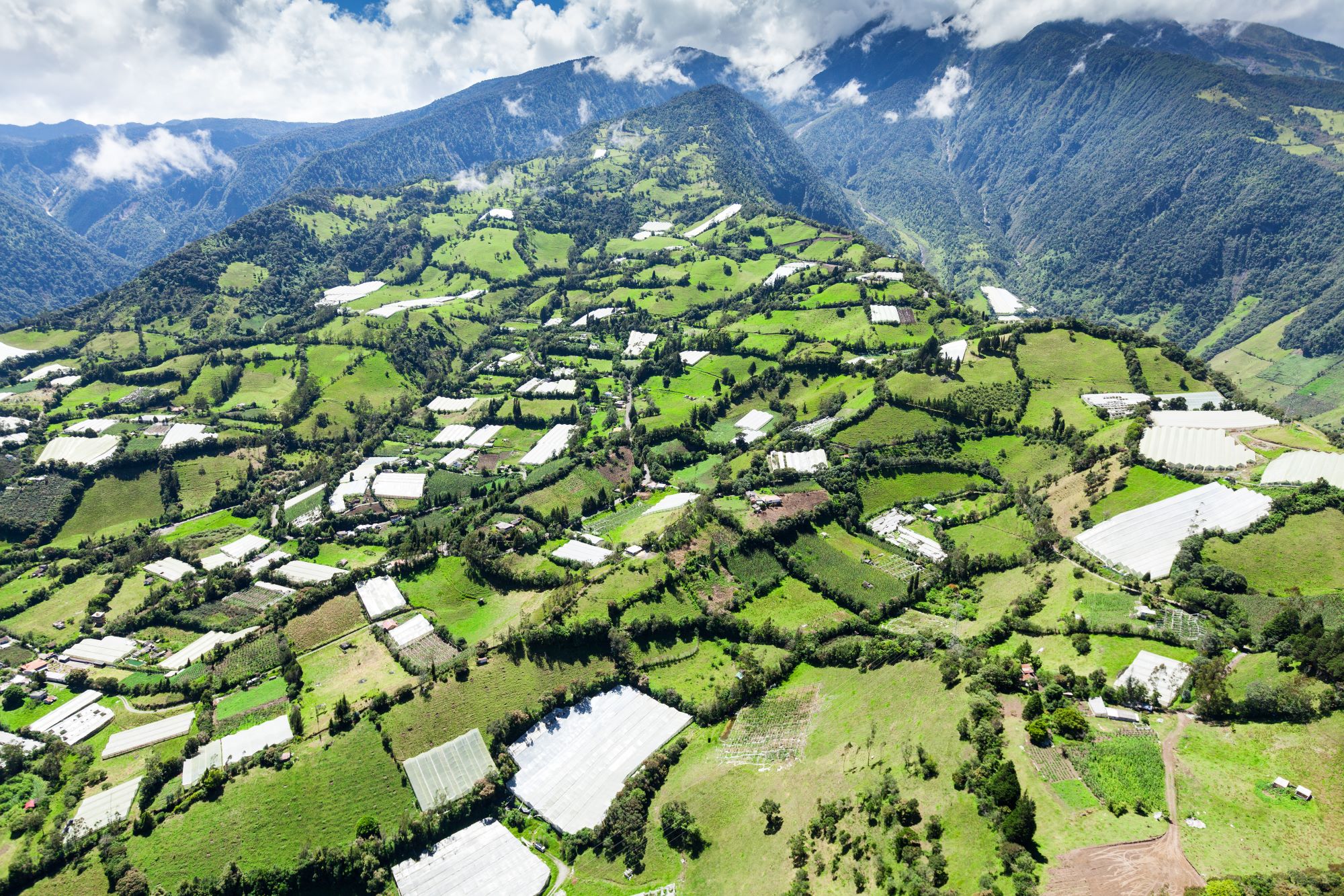 Zelena pokrajina na območju Runtun v bližini kraja Baños v Ekvadorju in vulkan Tungurahua v ozadju obdan z oblaki.