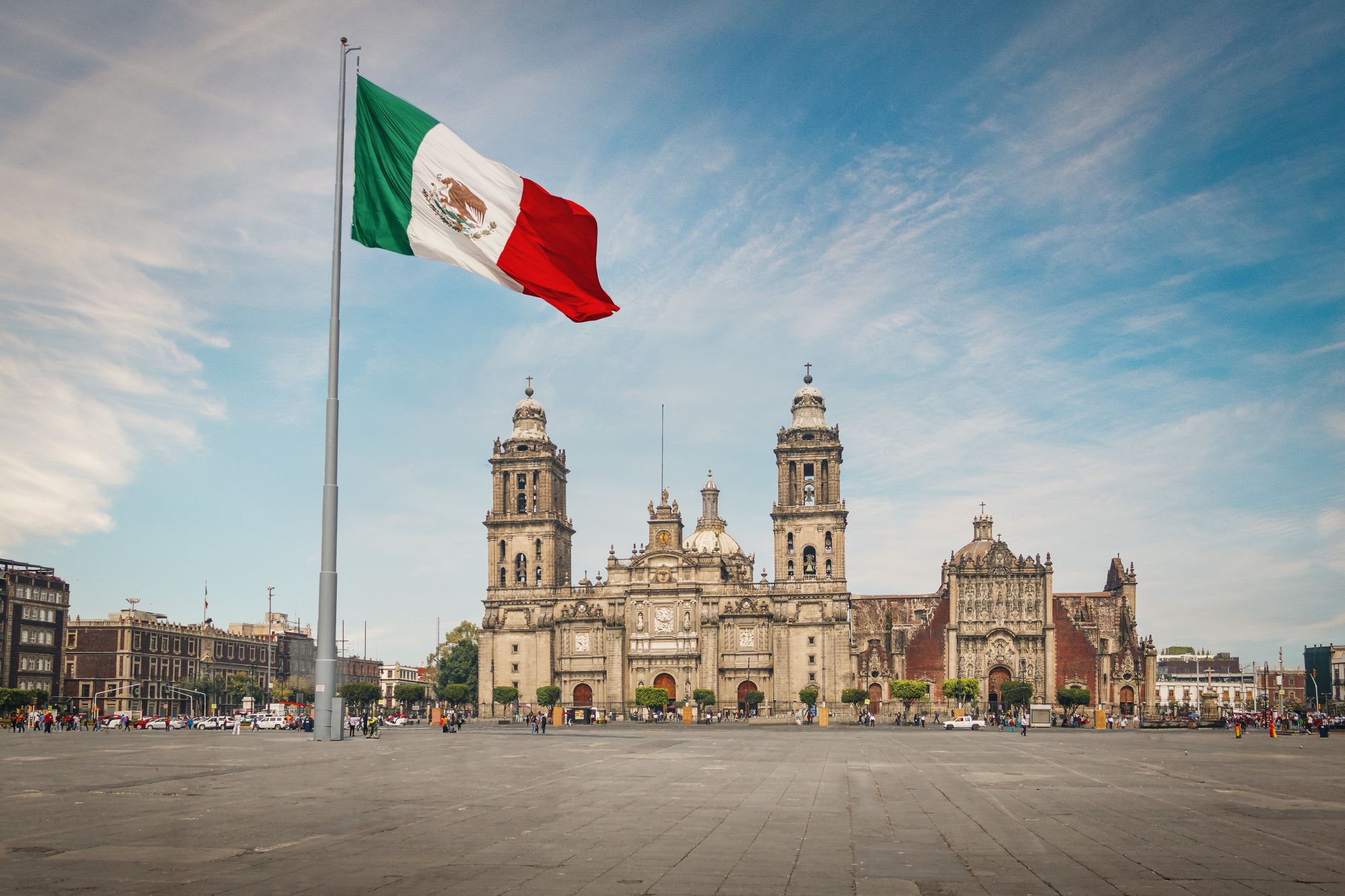 Mehiška zastava plapola na drogu na glavnem trgu mehiške prestolnice Ciudad de Mexico in v ozadju katedrala.