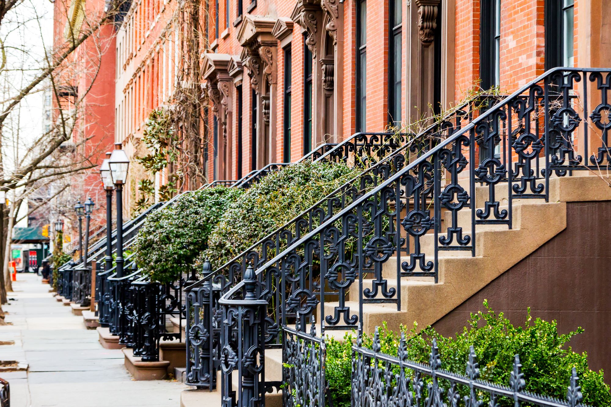 Stopnišča z okrašenimi kovinskimi ograjami, ki vodijo do vhodov v vrstne hiše na eni od ulic v newyorškem predelu Greenwich Village na Manhattnu.