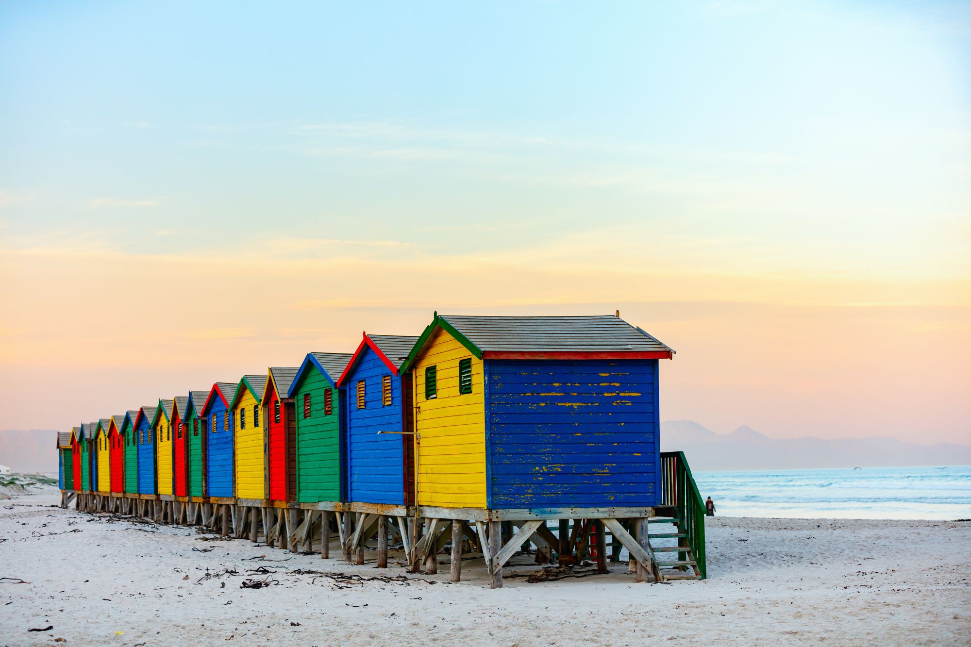 Slovite pisane hišice na plaži Muizenberg v Cape Townu v Južni Afriki in v ozadju zahajajoče sonce.