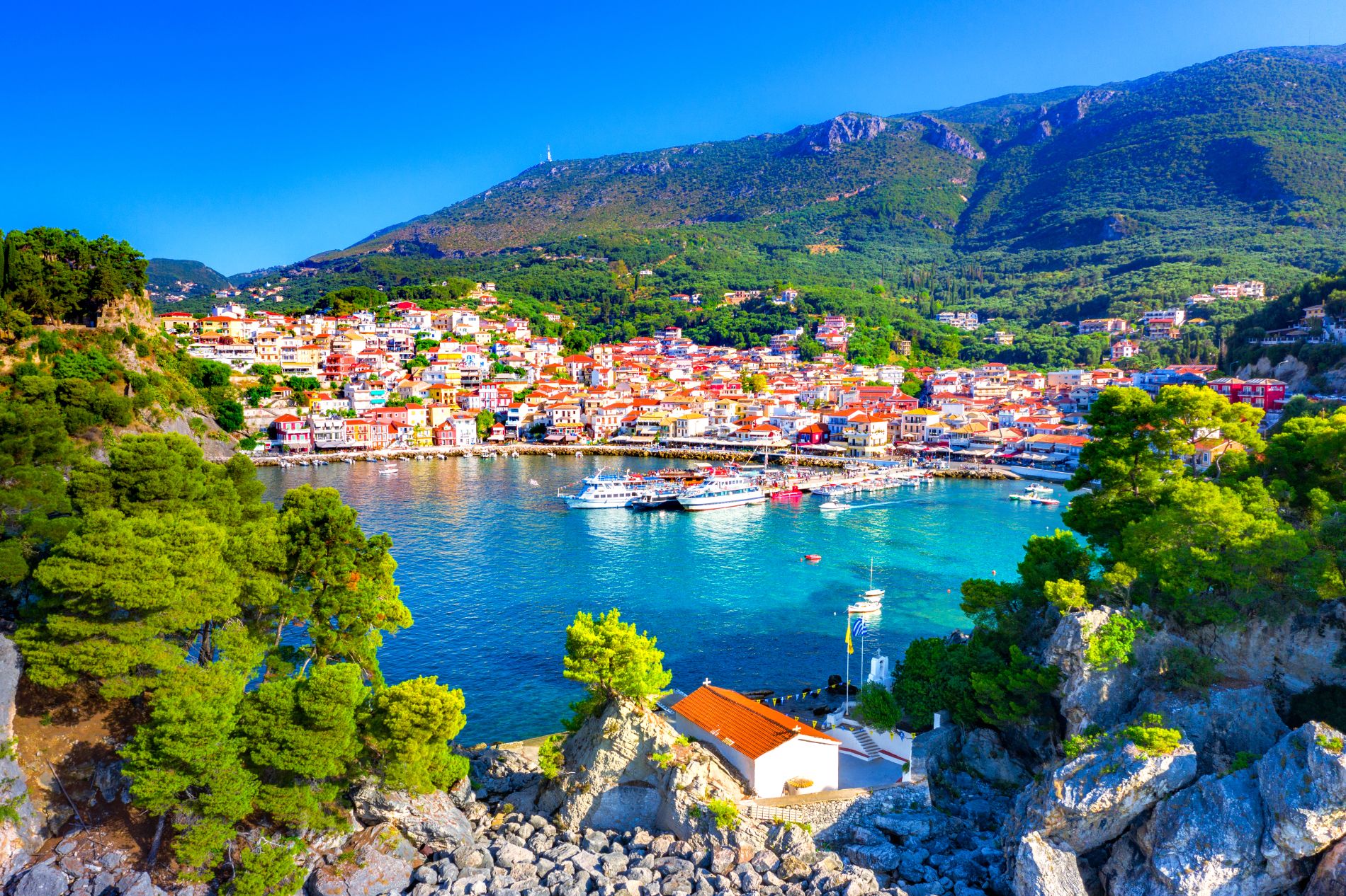 Panoramski pogled iz zraka na razgibano zeleno obalo Jonskega morja in slikovito obmorsko mestece Parga v Grčiji.