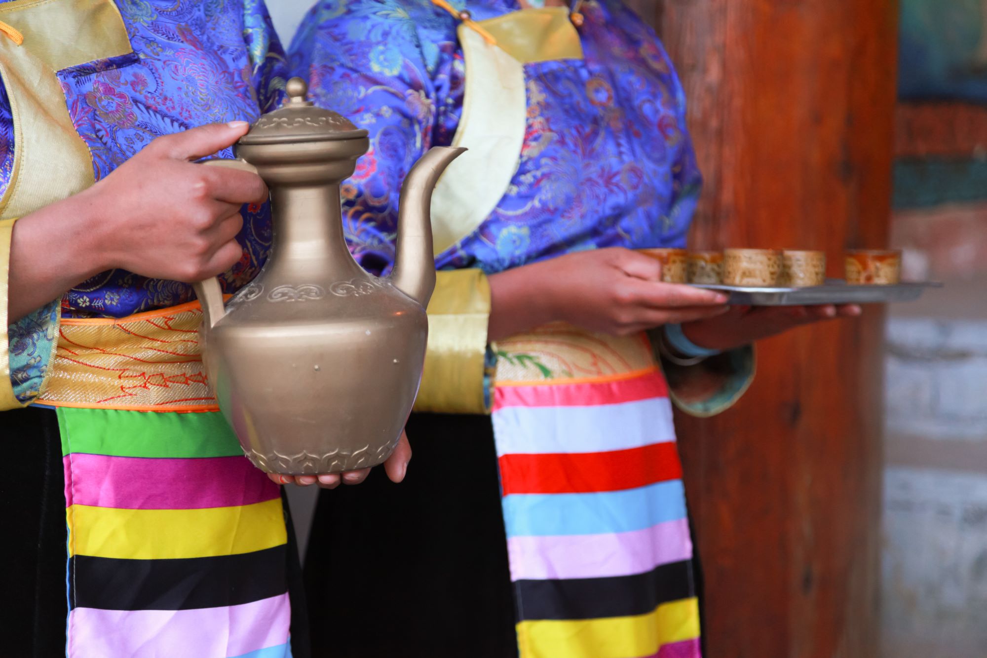Dve Tibetanki v tradicionalnih oblačilih strežeta čaj iz značilnega čajnika.