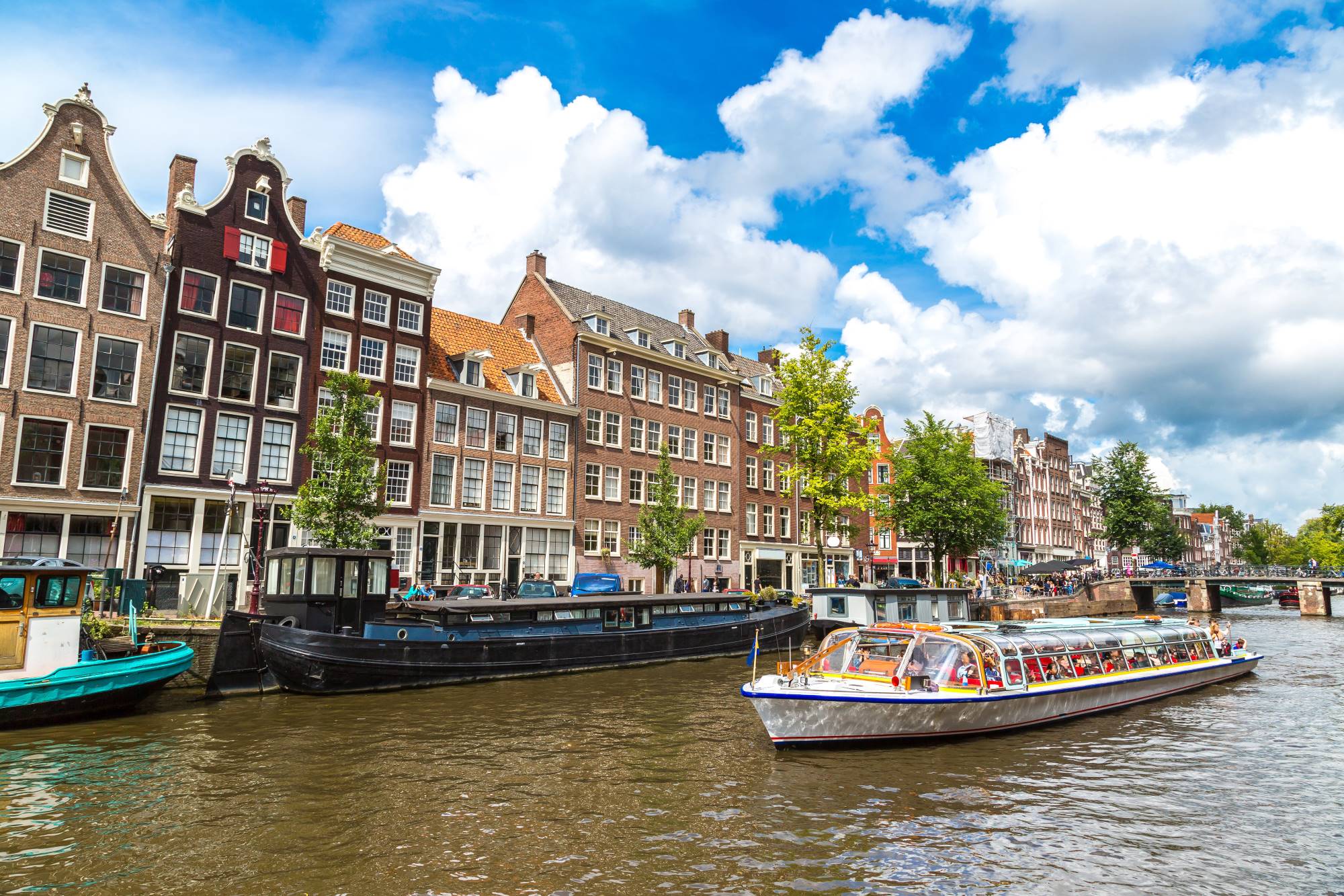 Vožnja s turistično ladjico po mestnih kanalih Amsterdama na Nizozemskem, ob katerem so zgrajene značilne ozke in visoke hiše.