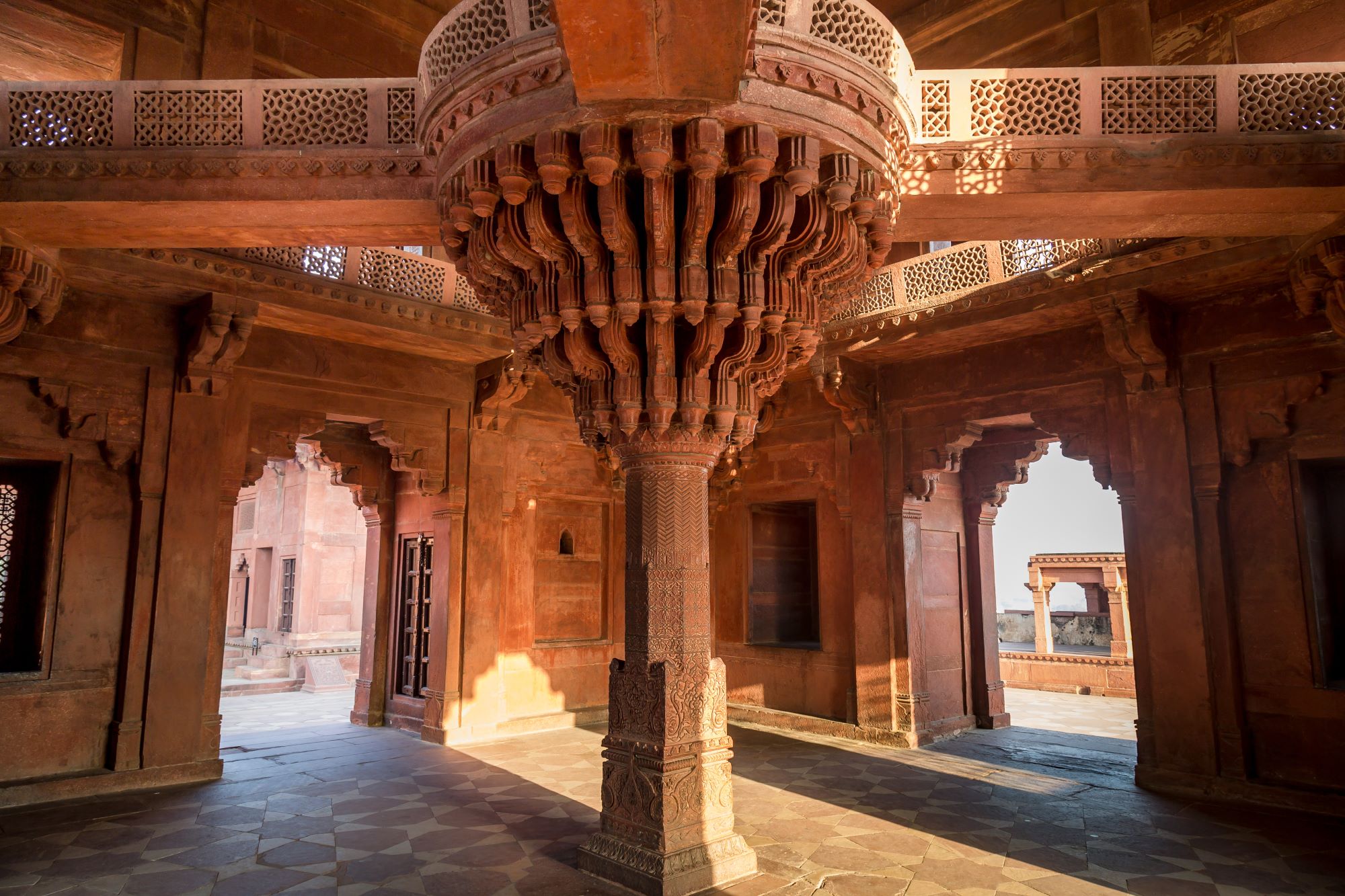 Pogled na nenavaden masiven lesen steber z umetelno izrezljano dekoracijo v sprejemni sobani Diwan-i-Khas v nekdanji vladarski palači v mestu Fatehpur Sikri v Indiji.