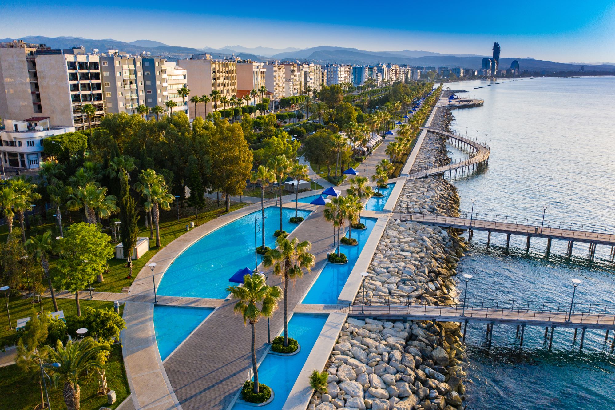 Pogled na moderno oblikovano promenado v Limassolu z drevoredom iz palm in modernimi stavbami v ozadju.