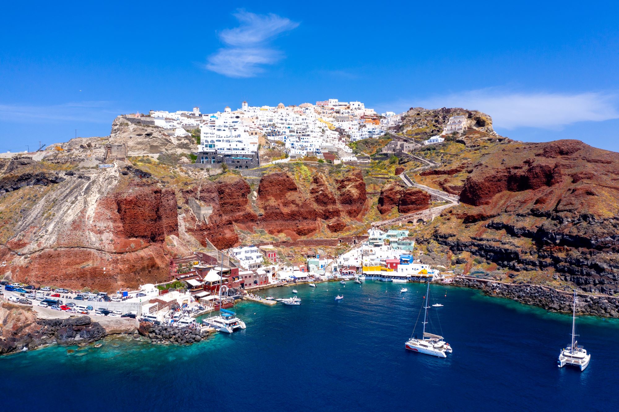 Pogled z morja na mestece Oia na otoku Santoriniju v Grčiji z belimi hišami, ki je zgrajeno na vrhu rdeče pečine.