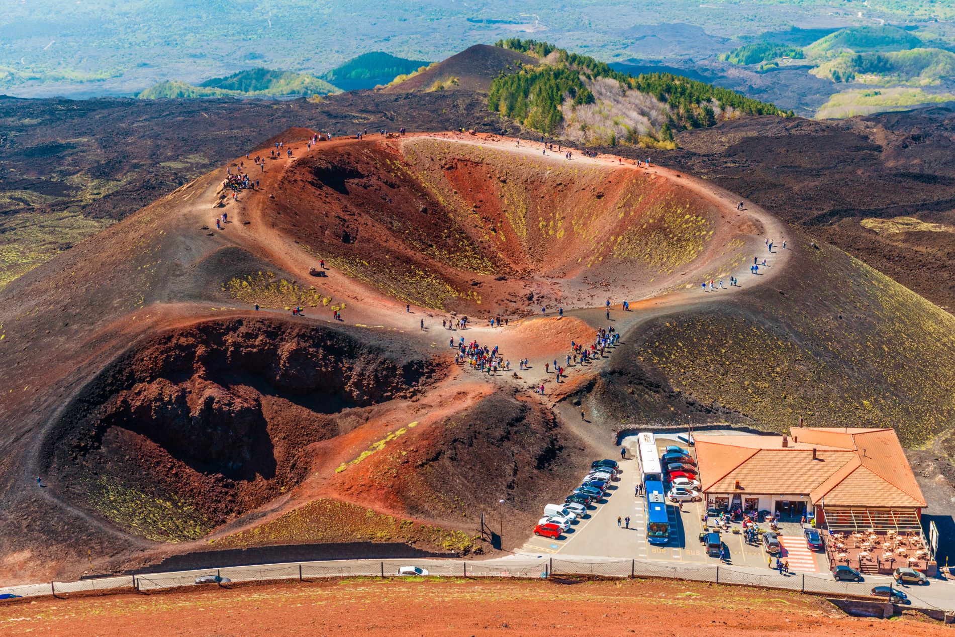 Posnetek iz zraka na postojanko na 2000 metrih nadmorske višine na vulkanu Etna z ugaslimi kraterji, po katerih se sprehajajo turisti.