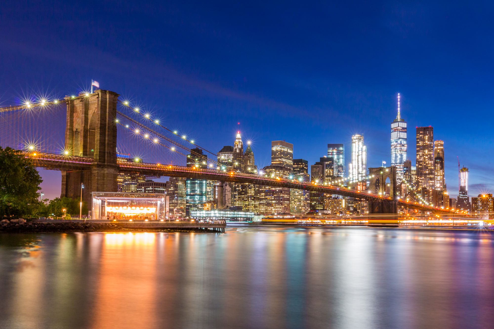 Osvetljen Brooklyn Bridge. V ozadju osvetljeni nebotičniki New Yorka.