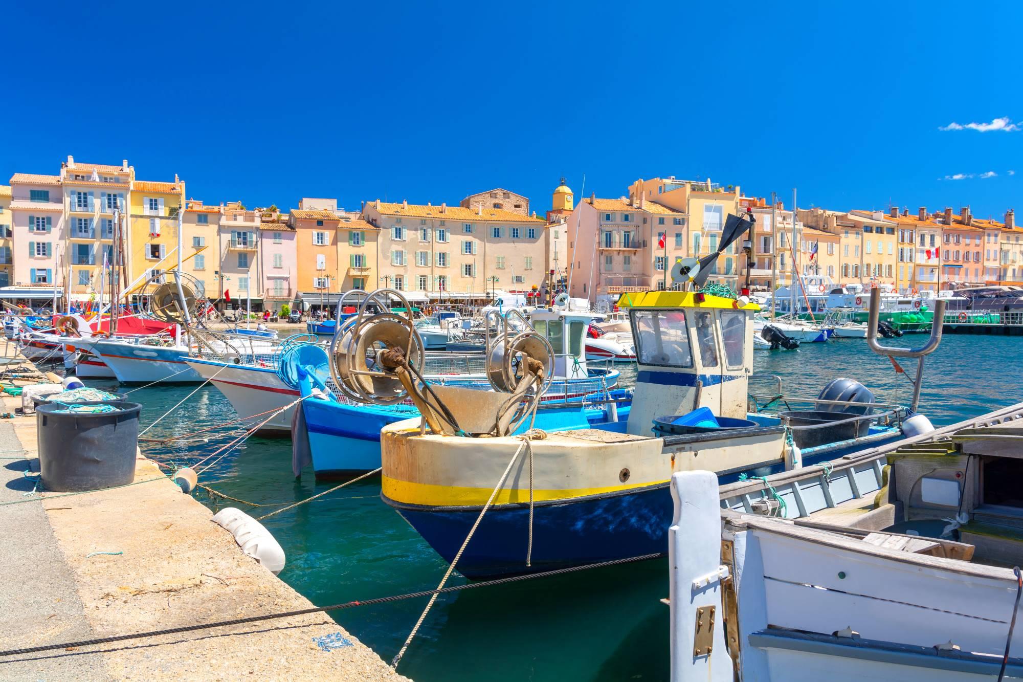 Ribiški čolni v marini letovišča St. Tropez in pogled na pisane hiše ob morju.