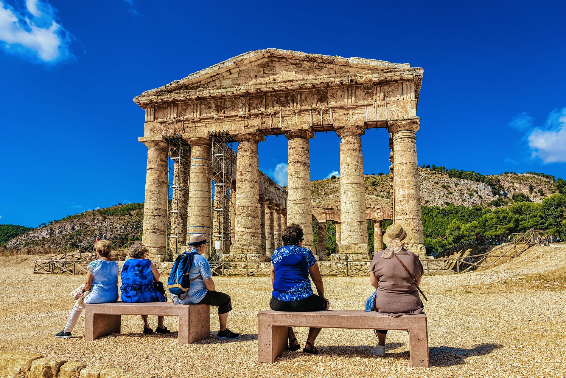 Turistke sedijo na klopeh in občudujejo neverjetno dobro ohranjen dorski tempelj Segeste na Siciliji.