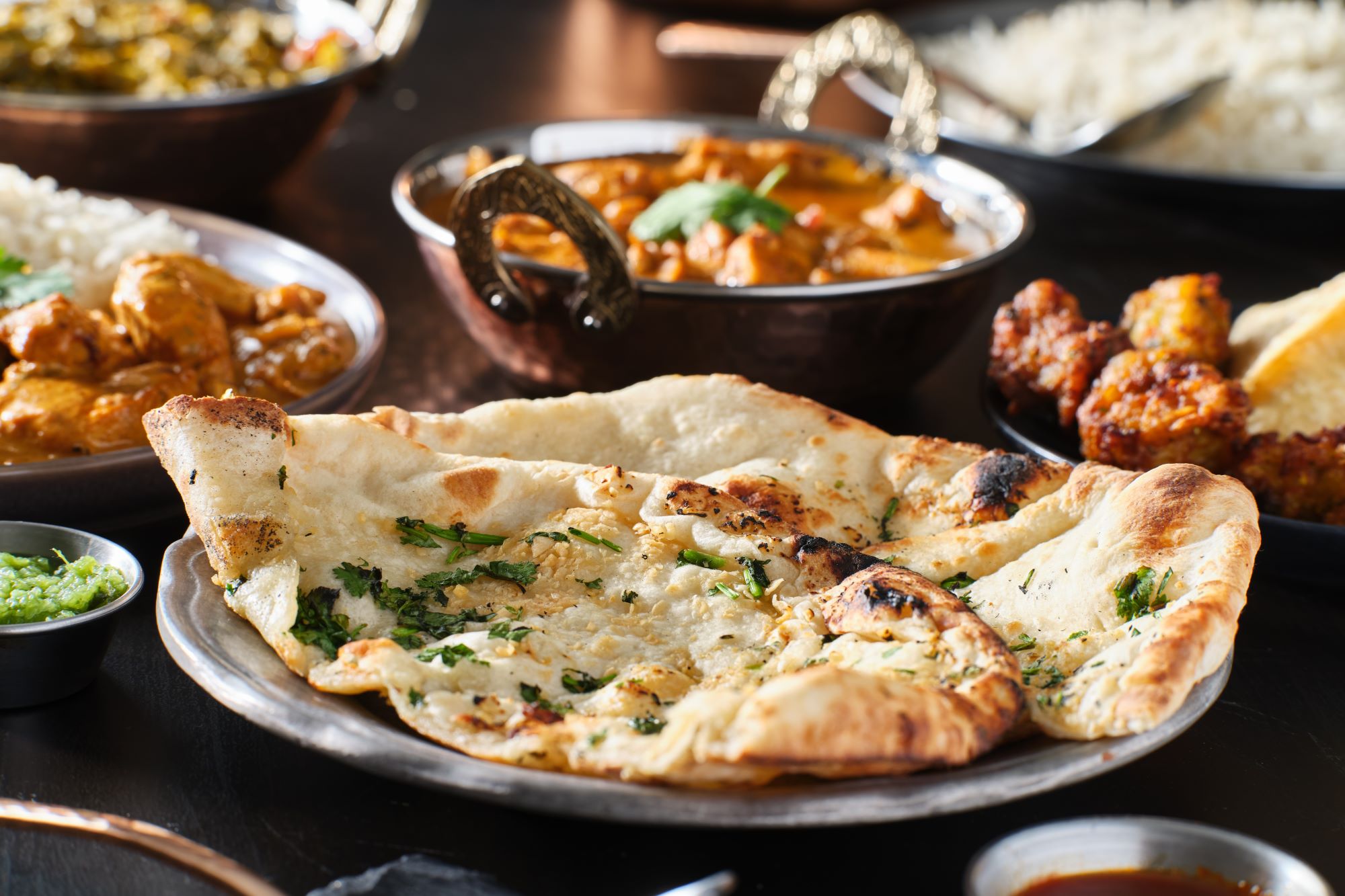 Pogled na obloženo mizo z značilno začinjeno indijsko hrano curry in ploščatim kruhom naanom.