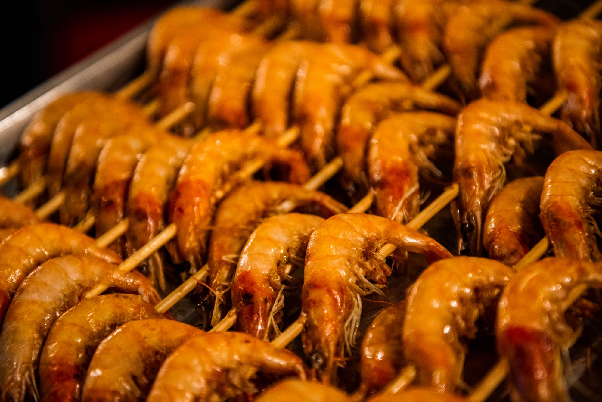 Nabodalca s kozicami na žaru v eni od uličnih prodajaln hrane v Pekingu na Kitajskem.
