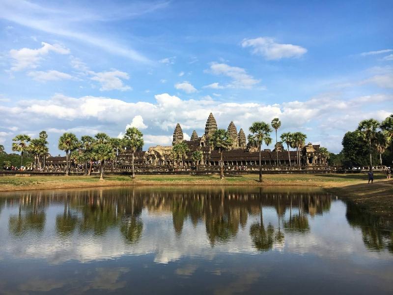Pogled na Angkor Wat, obdan z drevesi in modrim nebom ter oblaki.