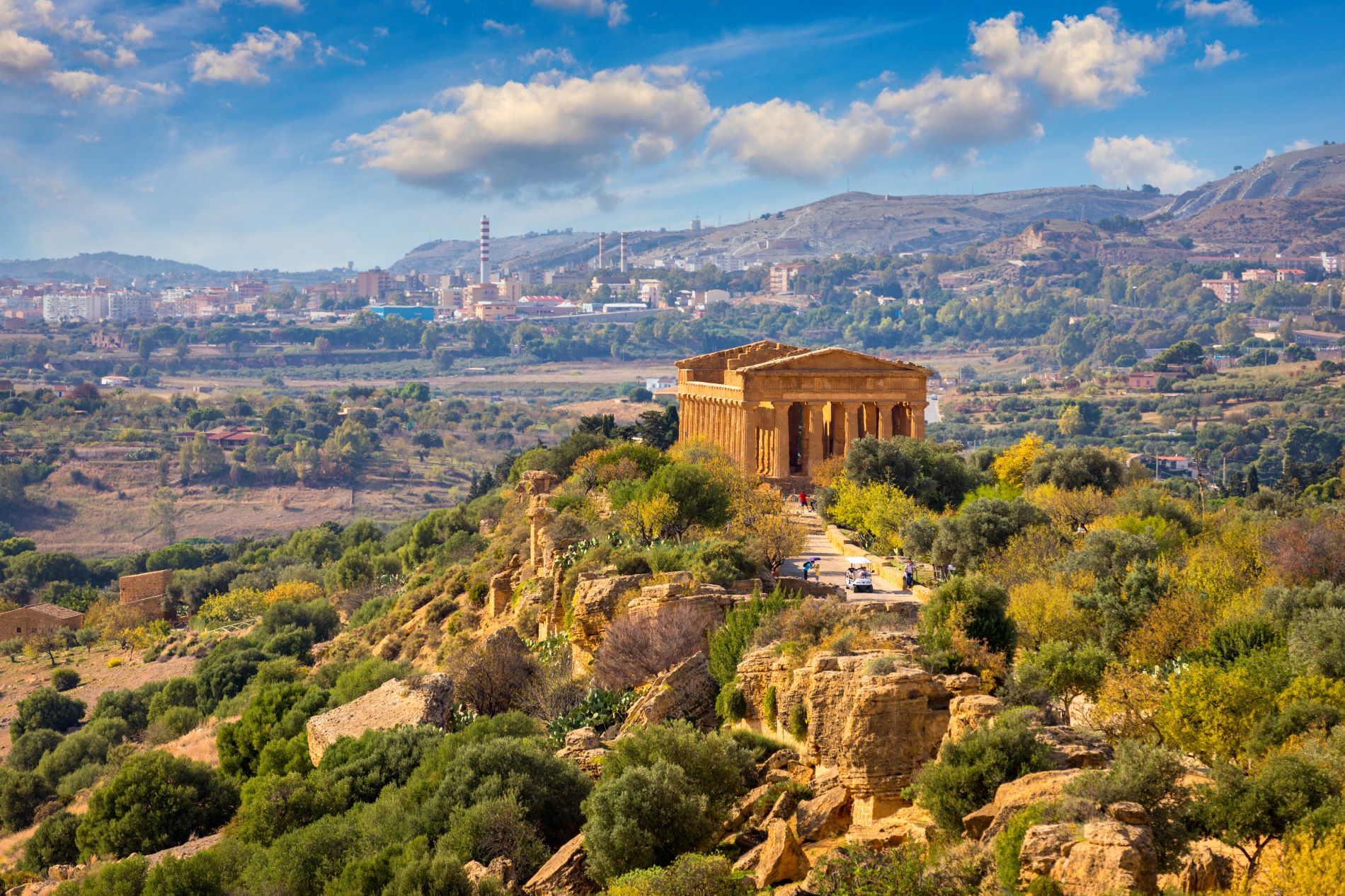 Pogled proti odlično ohranjenemu Konkordijinemu templju v Dolini templjev na Siciliji in v ozadju moderno industrijsko mesto Agrigento.