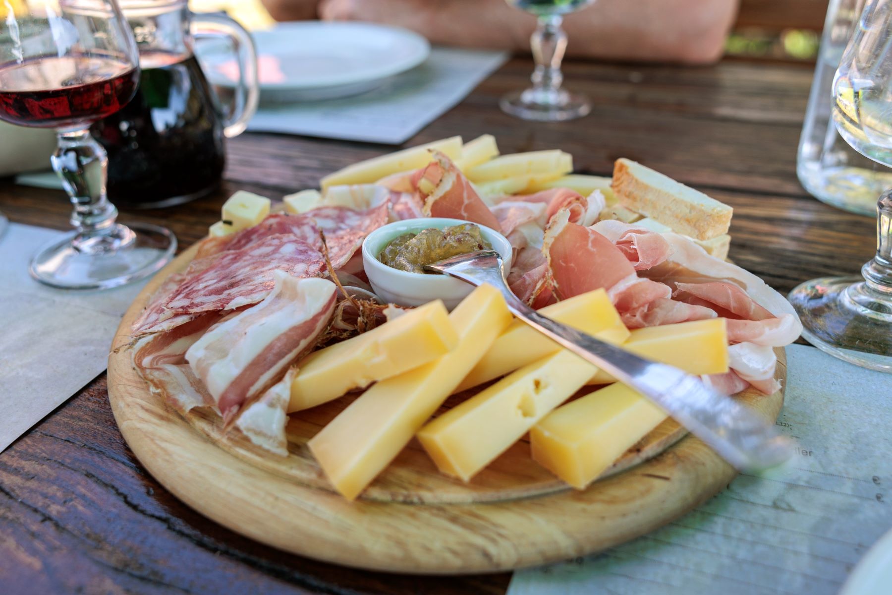 Domači siri in suhomesnati izdelki postreženi na leseni deski in degustacija rdečega vina na enem od kmečkih turizmov v Furlaniji v Italiji.