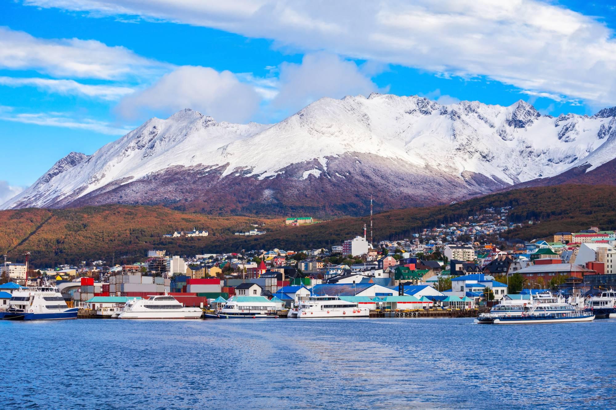 Pogled z morja na pristaniško mesto Ushuaia na Ognjeni zemlji in zasnežene gore v ozadju.