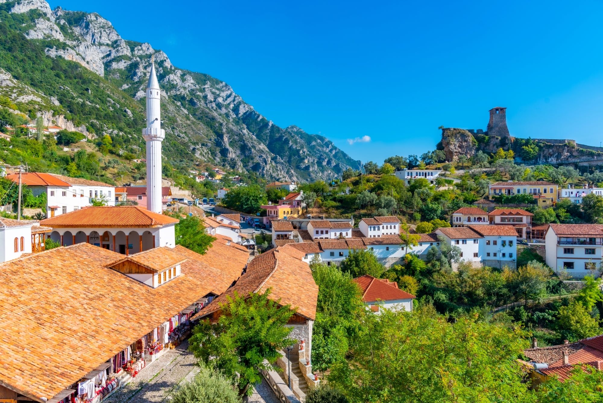 Pogled na stari del mesta Kruja v Albaniji z mošejo in mogočni grad na drugi strani vzpetine.