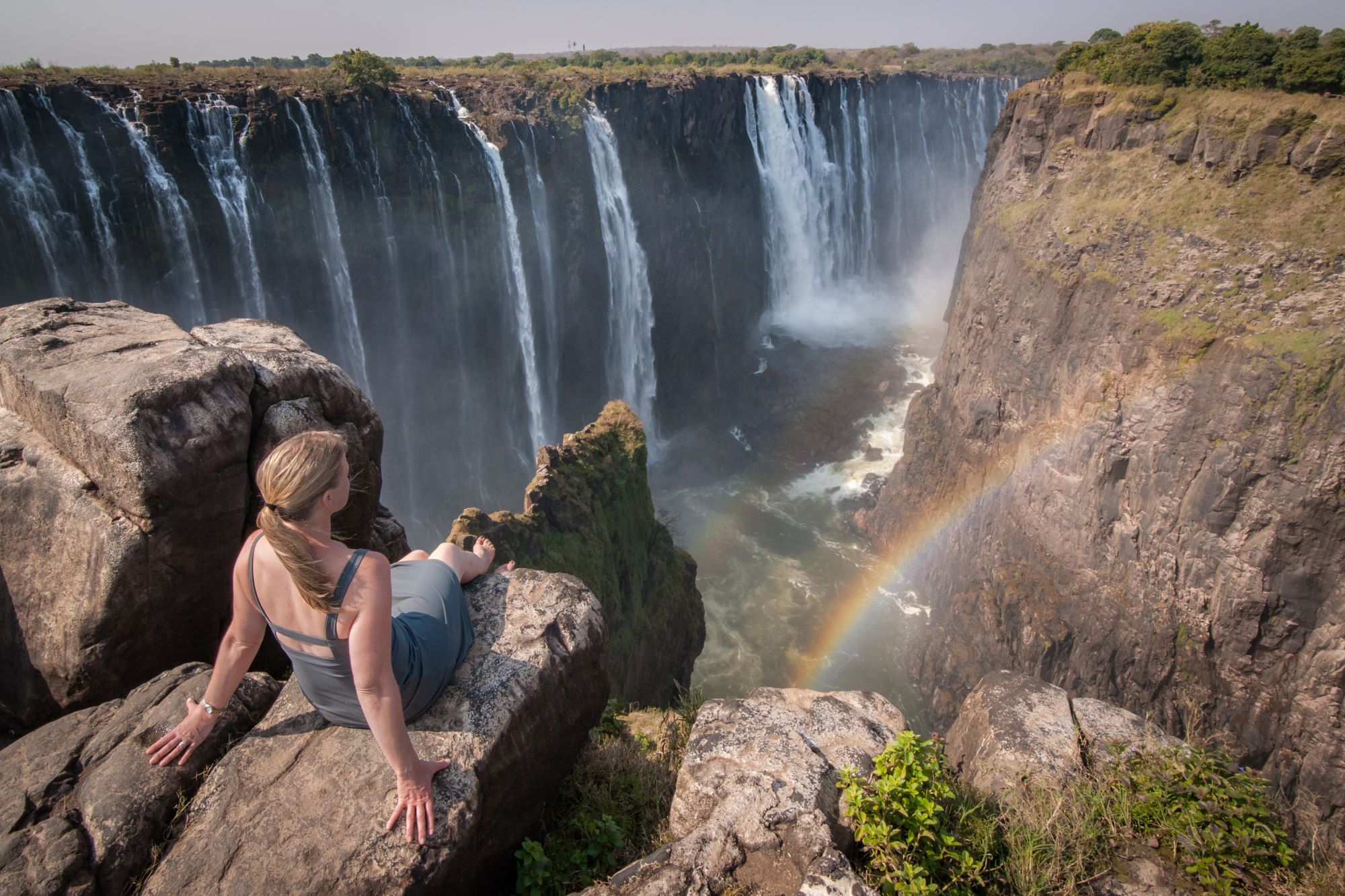 Turistka sedi na robu pečine z razgledom na mogočne Viktorijine slapove na reki Zambezi na meji med Zimbabvejem in Zambijo.