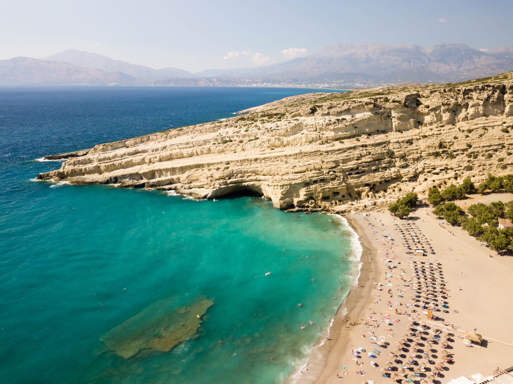 Plaža Matala na južnem delu Krete v Grčiji s turkiznim morjem in znamenito skalno steno, ki se spušča v morje.