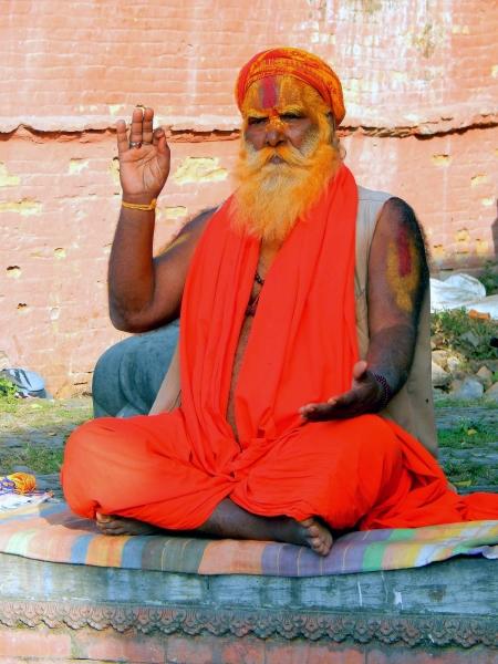 Nepalski sveti mož Sadhu v značilnih oranžnih oblačilih, okrašen z barvo po obrazu sedi pred najsvetejšim hindujskim templjem v Nepalu Pashupatinath v Katmanduju.