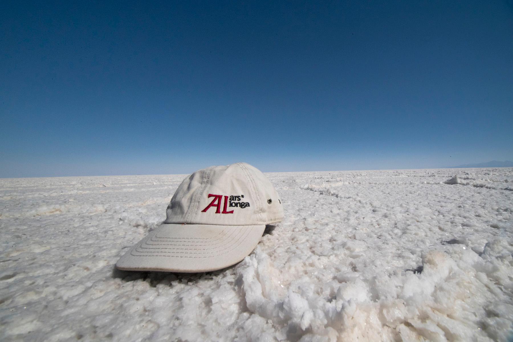 Kapa s šiltom z napisom Ars longa na slanih tleh presušenega jezera Salar de Uyuni v Boliviji.