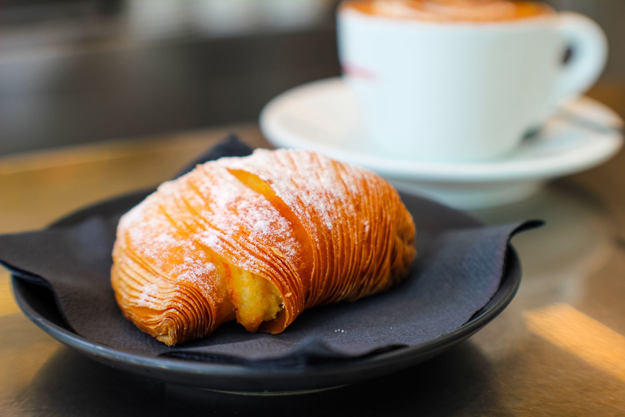 Sladica sfogliatella iz listnatega testa s sladkim nadevom iz rikote z aromo cimeta in pomarančnih cvetov, postrežena s kavo cappuccinom v baru v Neaplju.