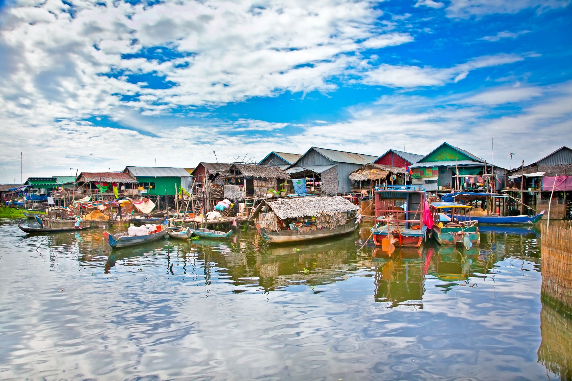 Plavajoče lesene hiše na vodi in pred njimi zasidrani čolni na jezeru Tonle Sap v Kambodži.