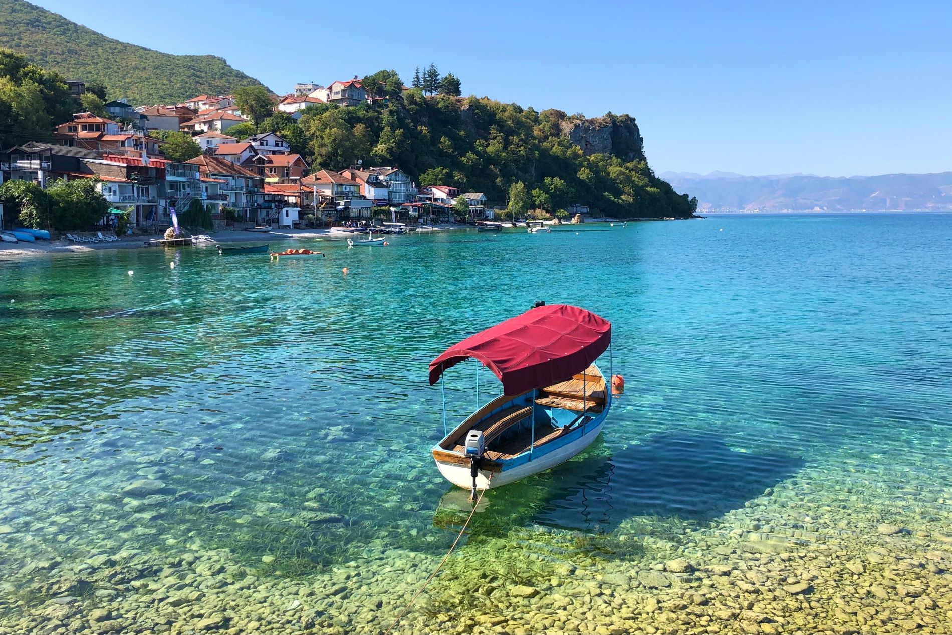 Mali čolnič je privezan na kristalno čisti modri vodi ob obali Ohridskega jezera v Severni Makedoniji.