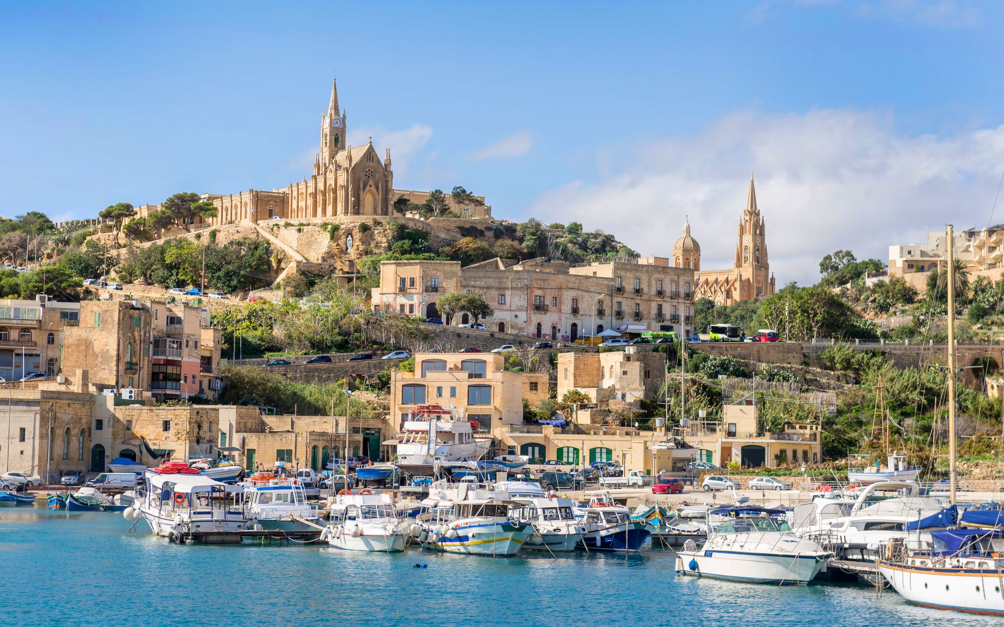 Zaliv Mgarr na malteškem otoku Gozo s pogledom na marino in Marijino cerkev na vzpetini nad morjem.