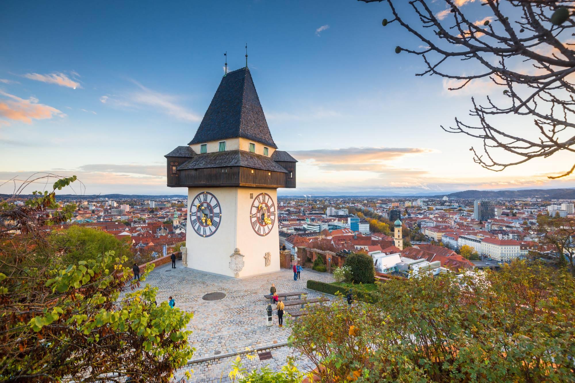 Urni stolp na Grajskem hribu v Gradcu na Avstrijskem Štajerskem v večerni svetlobi in pogled na mesto za njim.