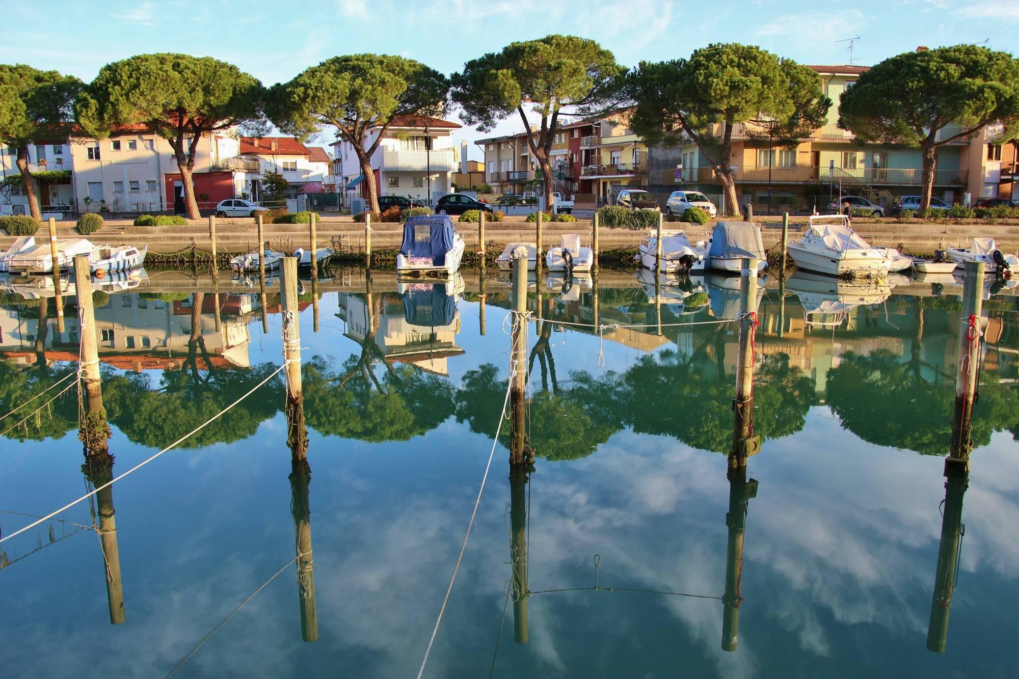 Eden od kanalov s privezanimi čolni v turističnem mestecu Gradež v Gradeški laguni na severu Italije ob Jadranskem morju.